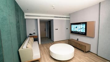 A modern bathroom with a round bathtub, a bench, a vanity with a mirror, and a wall-mounted TV displaying information.