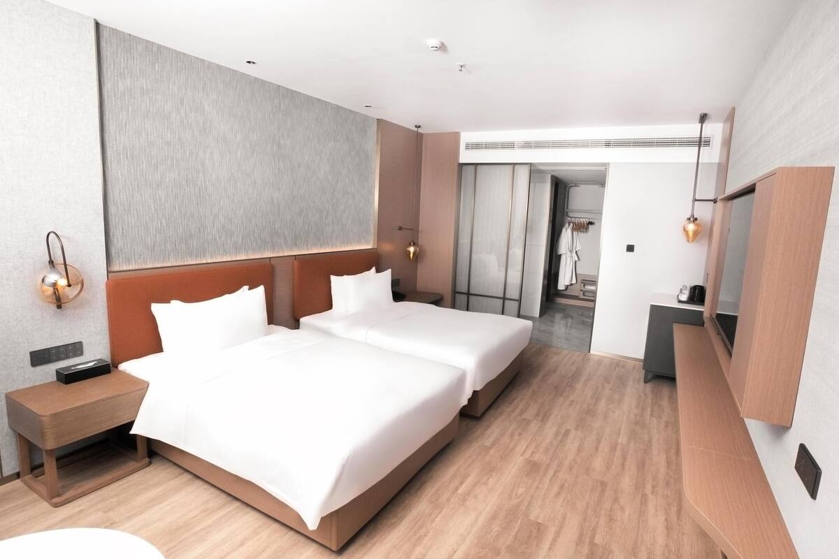 Ein modernes Hotelzimmer mit einem großen Bett, Nachttischen, einem Spiegel und Blick auf den Flur.