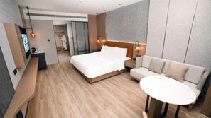 Een moderne hotelkamer met een bed, een bank, een kleine tafel, een televisie en een inloopkast.