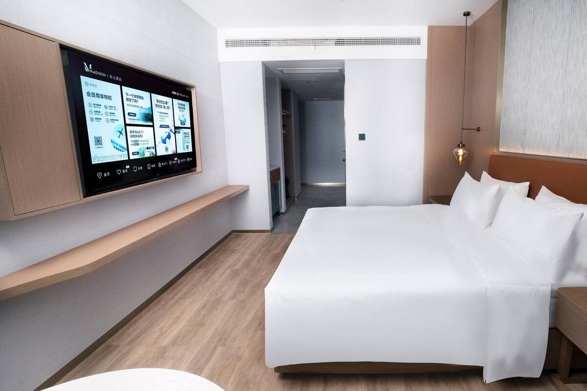 Ein modernes Hotelzimmer mit einem großen Bett, einem an der Wand befestigten Fernseher, einem Nachttisch und einem bei dem Bett stehenden Tisch.