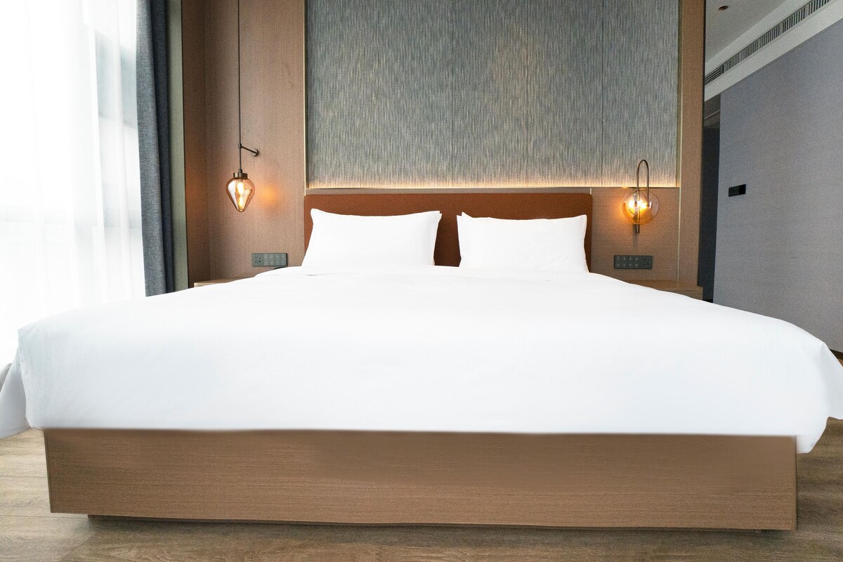 A large bed with a wooden frame, two wall-mounted light fixtures, and a textured wall behind the bed.