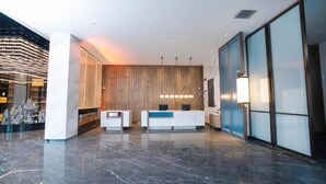 A modern reception area with marble flooring, a wooden wall panel, and a reception desk with a computer monitor.