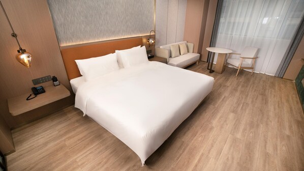 A hotel room with a large bed, bedside tables, a sofa, a small table, and a wall-mounted lamp.
