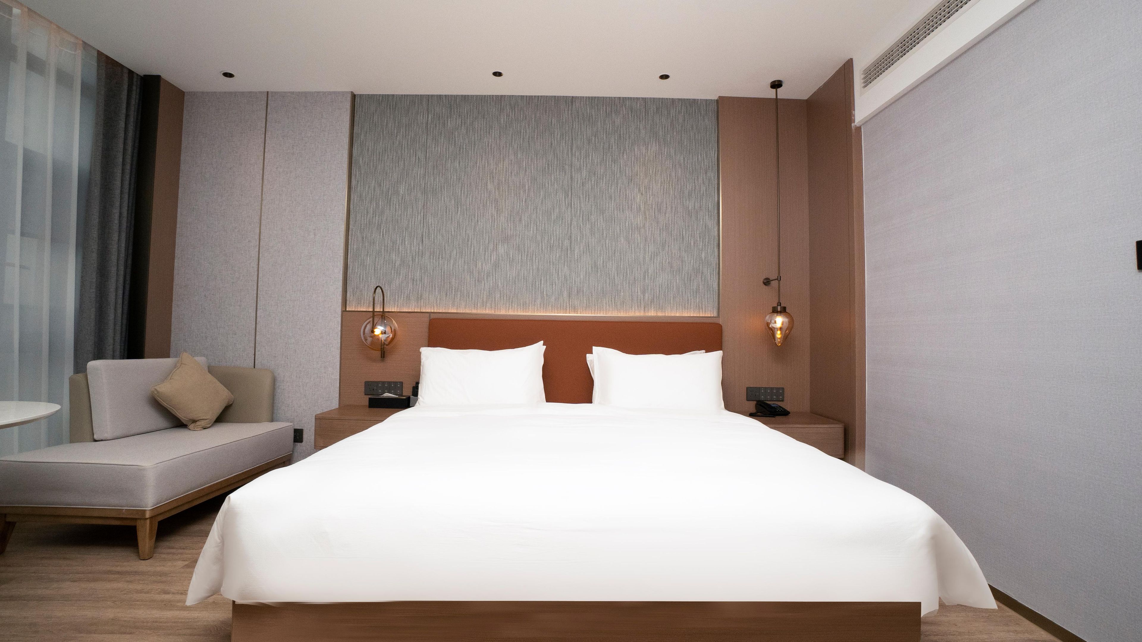 Una habitación de hotel moderna con una cama grande, un sofá, una mesita de noche y una lámpara fijada a la pared.