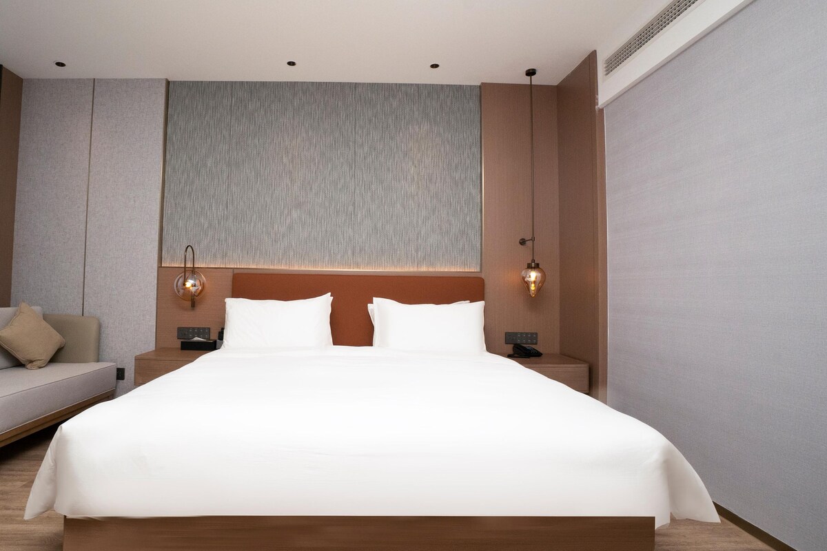 Une chambre d’hôtel moderne, dotée d’un grand lit, d’un canapé, d’une table de chevet et d’une lampe fixée au mur.