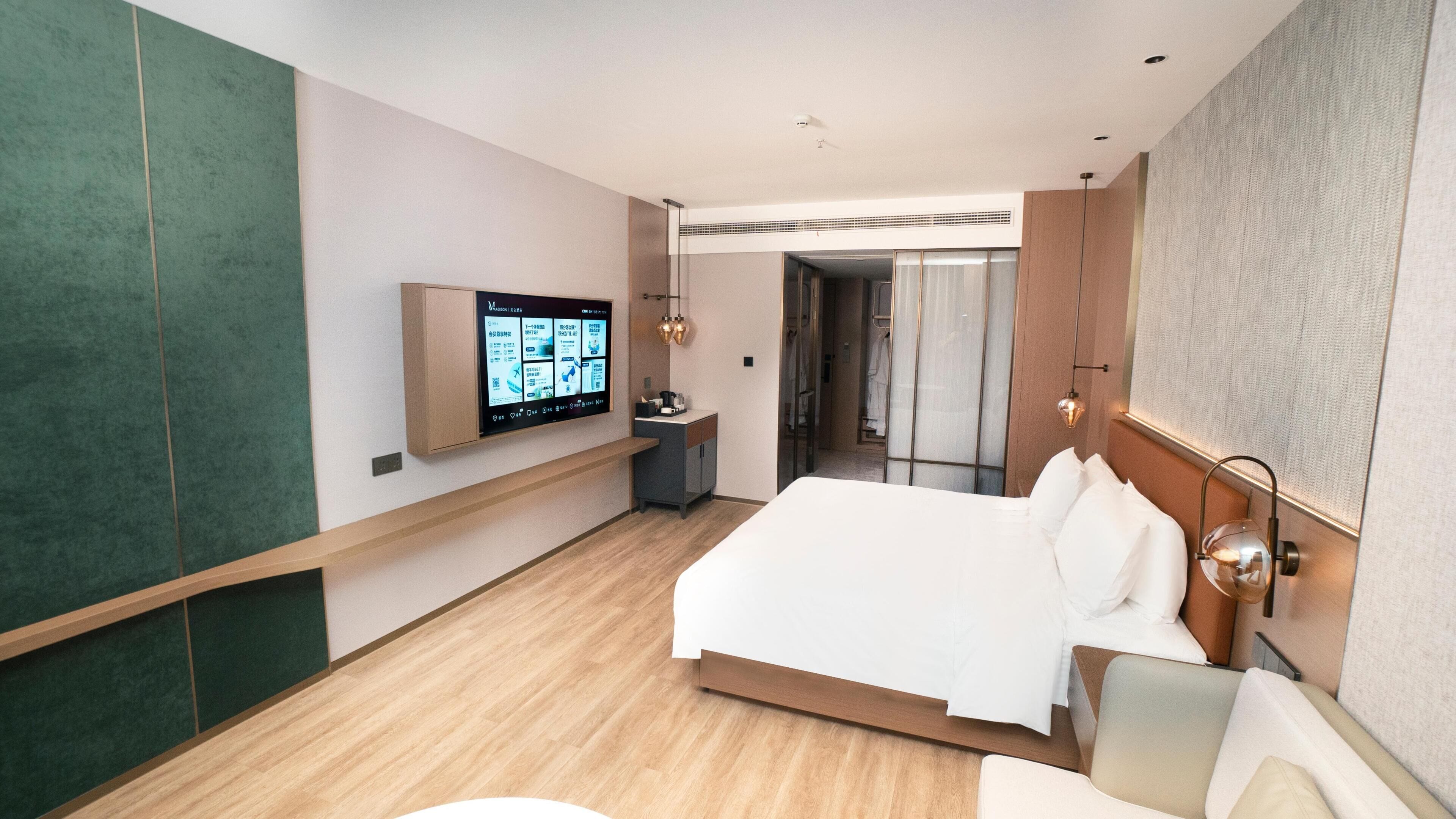 A modern hotel room with a large bed, a TV mounted on the wall, a desk, and a walk-in closet.