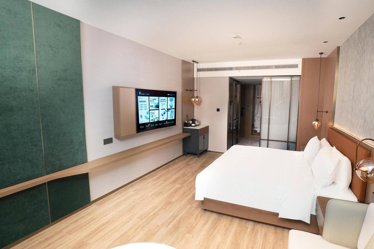 Ein modernes Hotelzimmer mit einem großen Bett, einem an der Wand befestigten Fernseher, einem Schreibtisch und einem begehbaren Kleiderschrank.