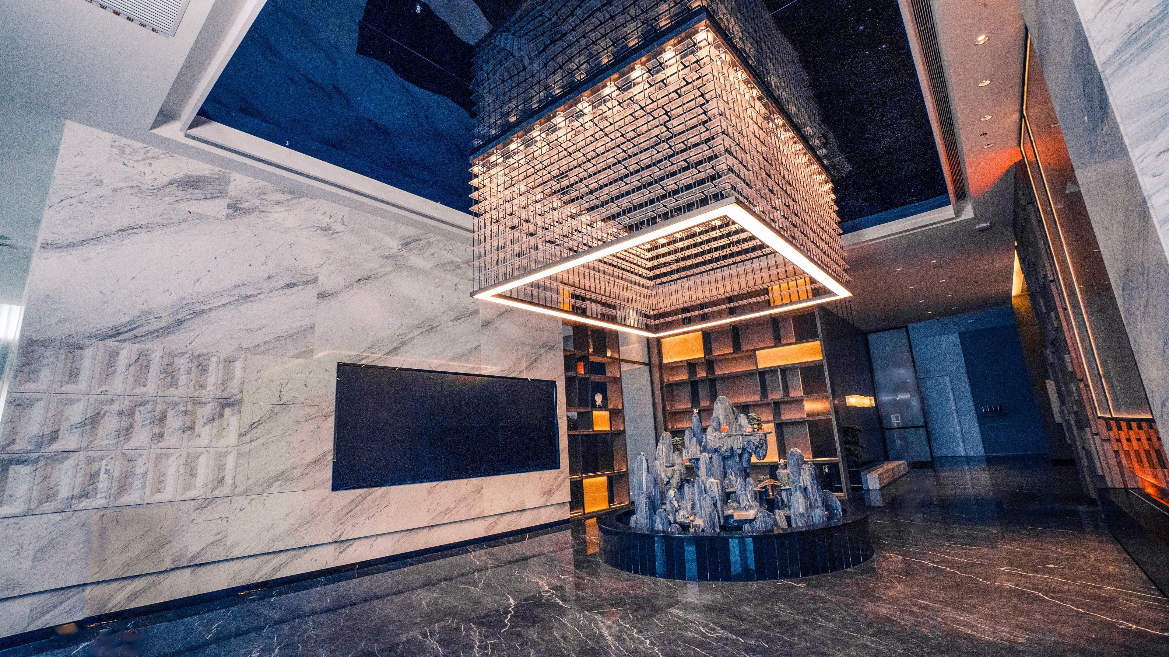 A lobby with a marble floor, a central fountain, and a modern brick wall with illuminated shelves.