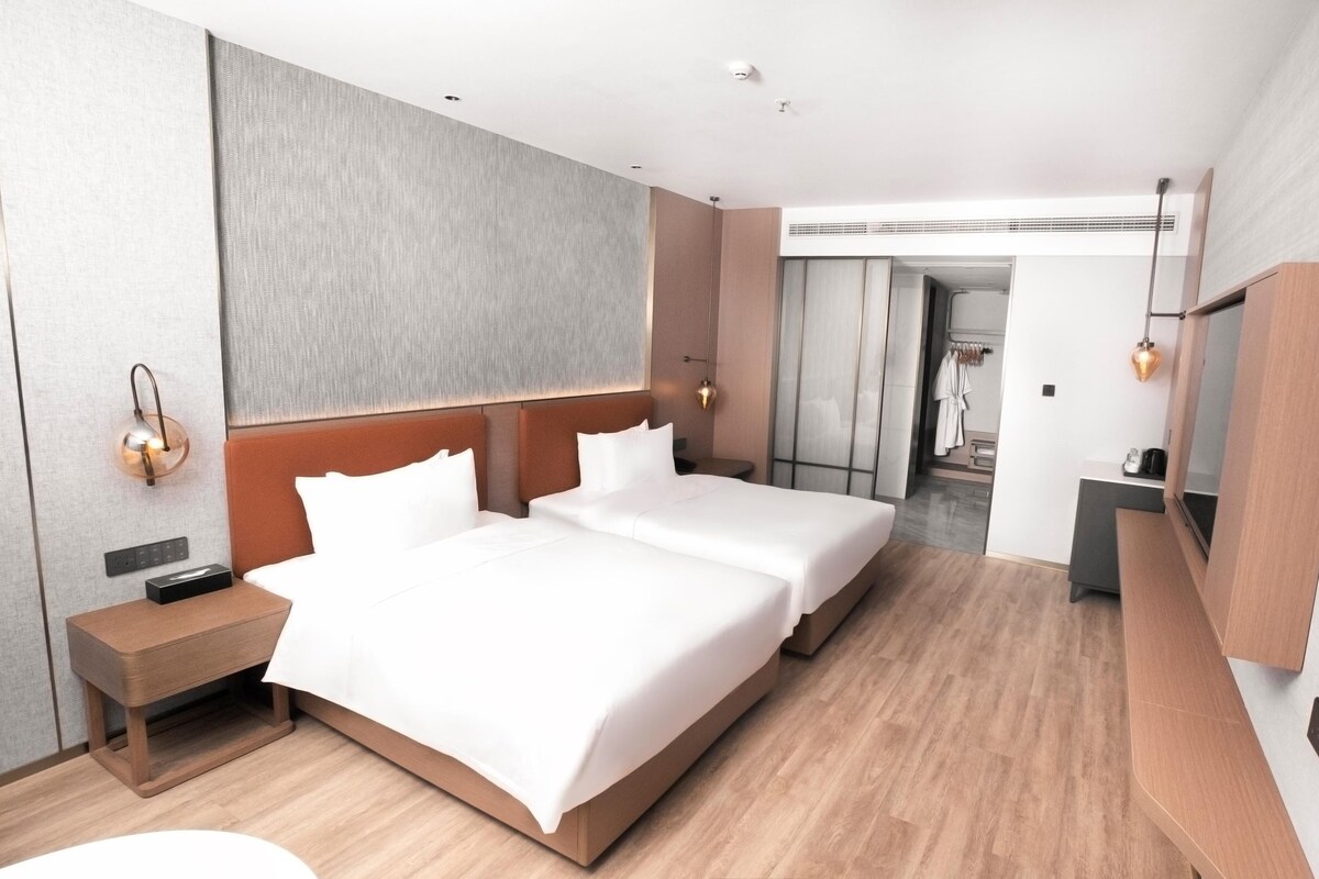 A modern hotel room with a large bed, bedside tables, a mirror, and a view of the hallway.