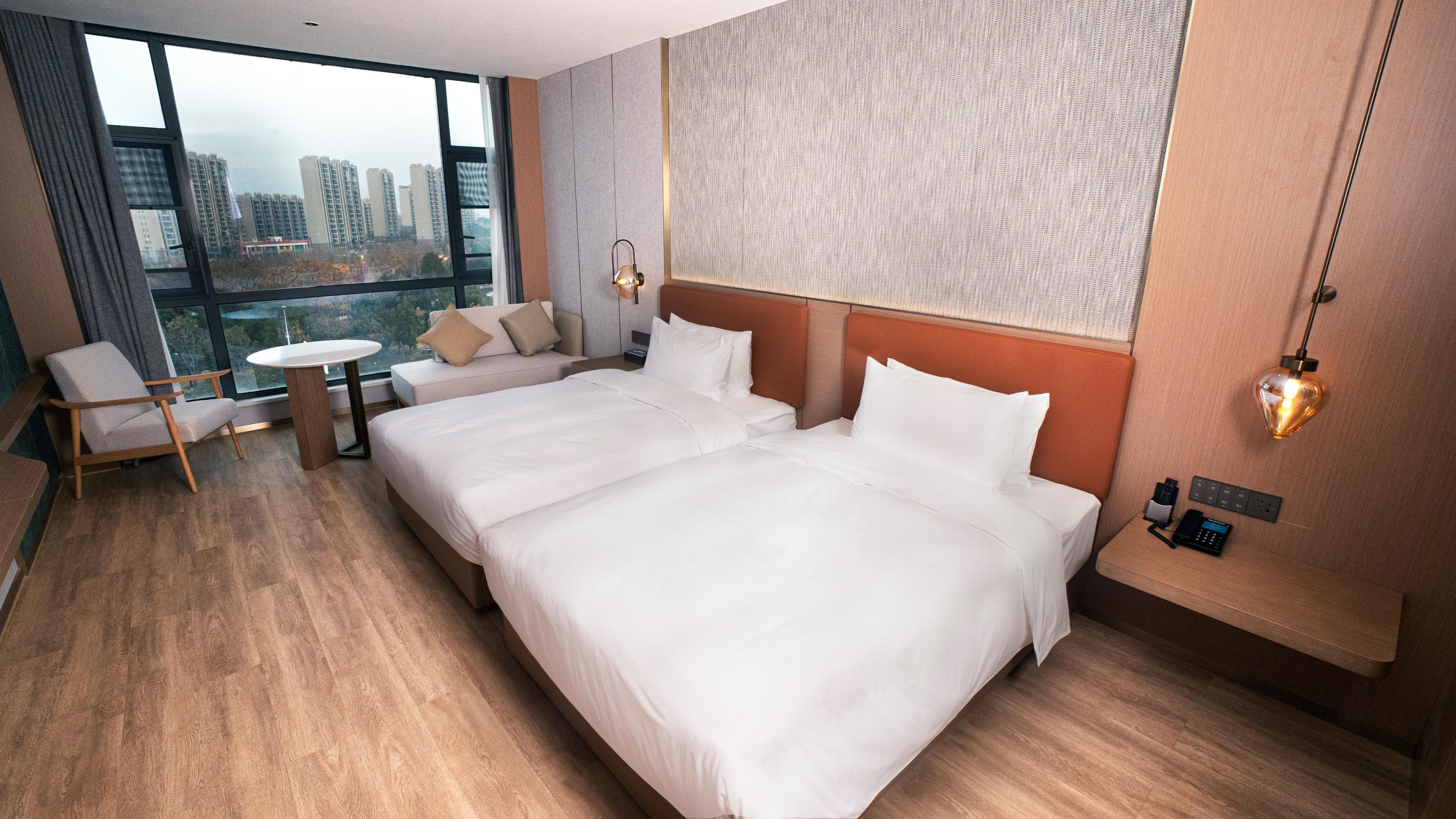 A hotel room with a large bed, a seating area with a table, and a view of tall buildings through the window.