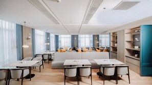 A modern dining area with tables and chairs, a central seating area, and a bookshelf.