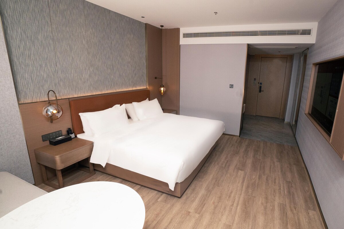 A hotel room with a bed, bedside table, lamp, and a TV mounted on the wall.