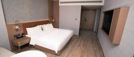 Quarto de hotel com cama, mesa de cabeceira, luminária e televisão na parede.
