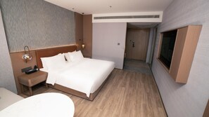 A hotel room with a bed, bedside table, lamp, and a TV mounted on the wall.