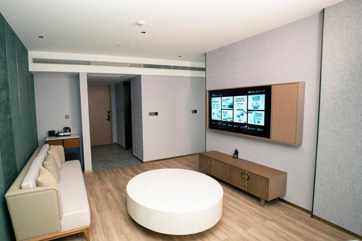 Ein modernes Badezimmer mit einer runden Badewanne, einer Sitzbank, einem Waschtisch mit Spiegel und einem an der Wand montierten Fernseher, der Informationen zeigt.