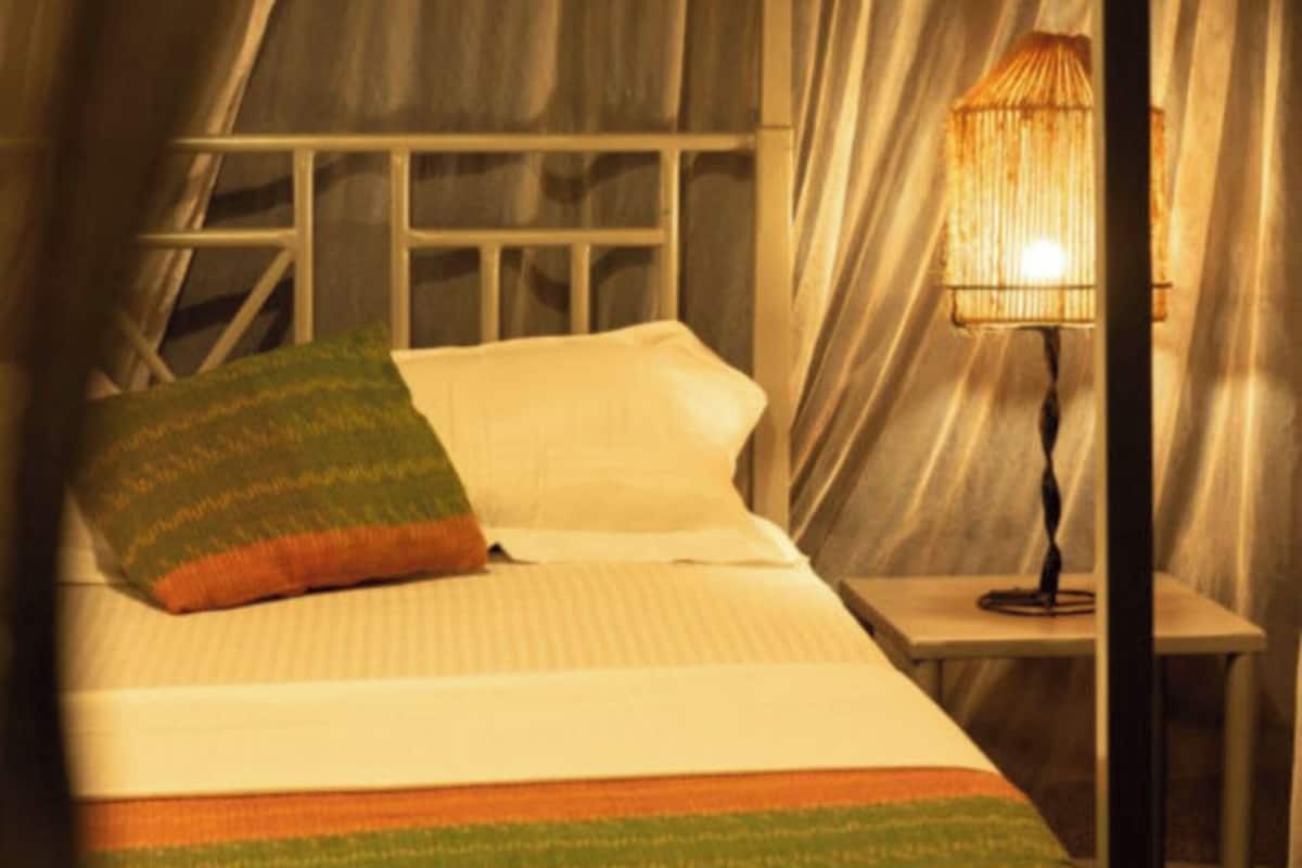 Un lit avec une couverture à rayures, un oreiller et une lampe de chevet, dans une pièce où sont accrochées des rideaux.