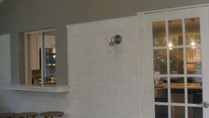 A room with a white brick wall, a large window, and a door with glass panels. There are three stools and a ceiling light fixture. - Modern Seaside Beach Retreat (Saint Helena Island)