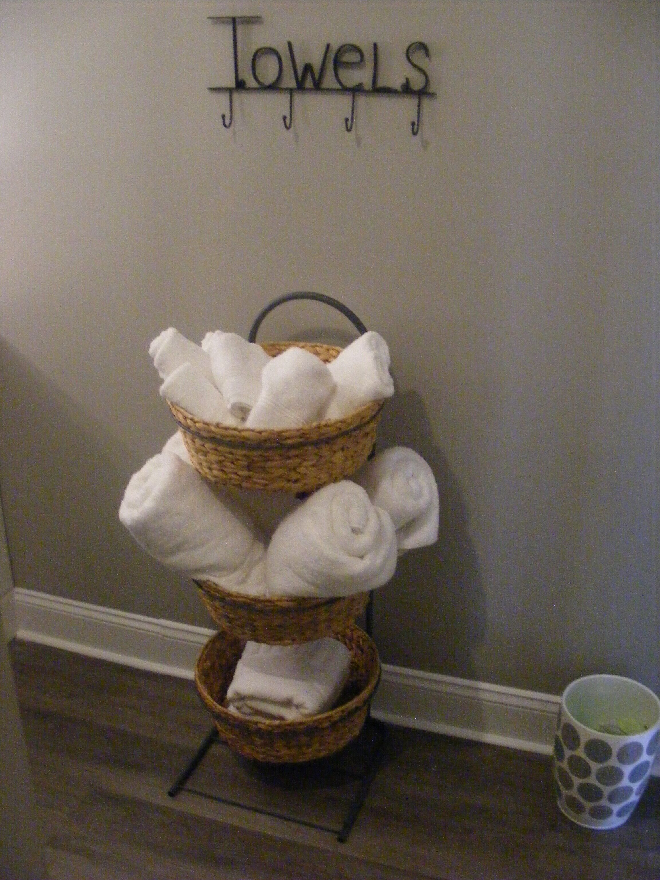 A wall-mounted towel rack with three wicker baskets holding folded towels.