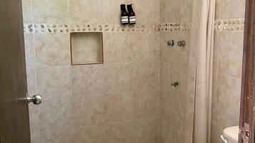 Ducha con azulejos color beige, cabezal de ducha, toallero con botellas y un inodoro.