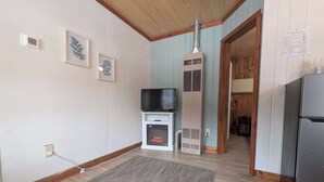 A room with a fireplace, a television, a refrigerator, and a door leading to another room. - Cozy 1BR 1BA Cabin #4 Riverside Point Resort (Park Rapids)