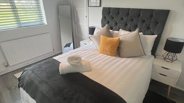 A modern bedroom with a large bed, a bedside table, a floor lamp, and a window with blinds. - 1 Bed Apartment - Sleeps 3 - Wifi - Parking (Wolverhampton)