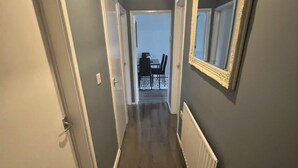 A narrow hallway with a door on the left, a radiator on the right, and a dining area visible through an open door at the end. - 1 Bed Apartment - Sleeps 3 - Wifi - Parking (Wolverhampton)