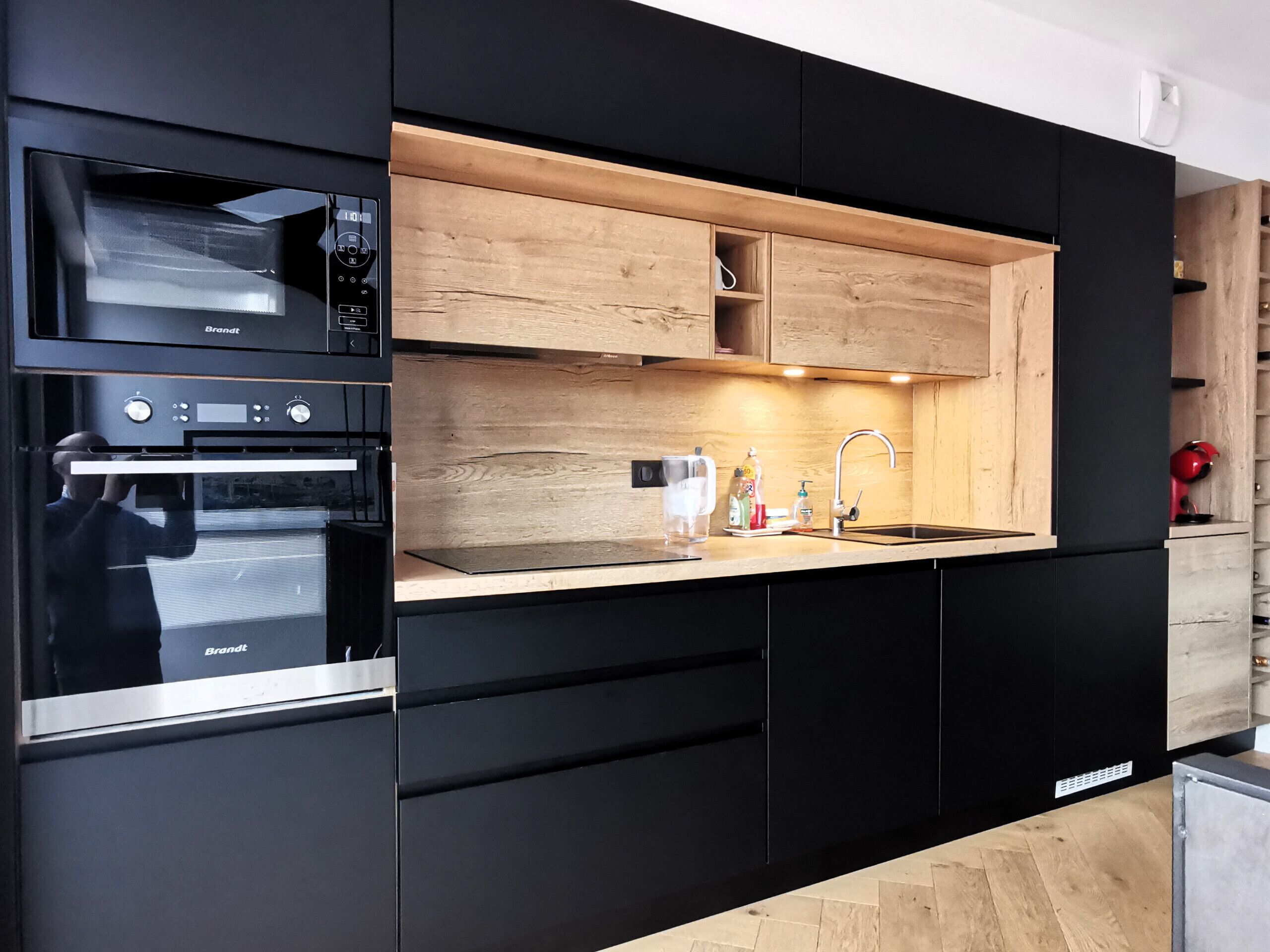 Una cocina moderna con armarios negros, encimera de madera, horno empotrado y un lavabo con grifo.