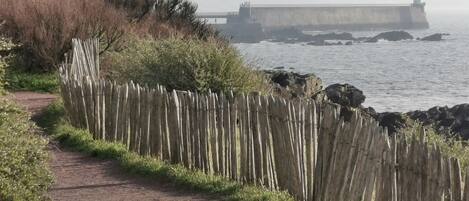 A coastal path with a wooden fence, a brick walkway, and a lighthouse in the distance.