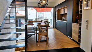 A modern kitchen with wooden flooring, a dining area with a table and chairs, and a staircase with black railings.