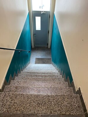 Un escalier aux murs bleus, doté d’une rampe, qui mène à une porte avec une fenêtre.