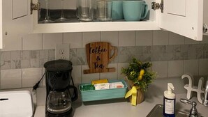 Una cucina con mobili bianchi, una macchina da caffè, un lavello e un cartello con su scritto 'Coffee & Tea'.