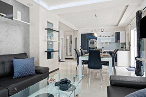 Ein modernes Wohnzimmer mit einem Glastisch, einer schwarzen Ledersofa und einem Essbereich mit Glastisch und Stühlen.
