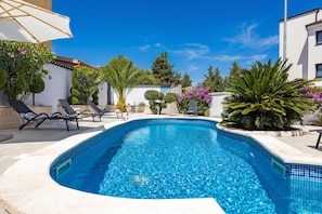Una piscina con lettini, circondata dal verde e da un cielo azzurro limpido.