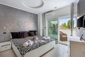 Una camera da letto moderna con copriletto a fantasia zebrata, una porta in vetro che dà su un balcone e un televisore a parete.