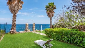 A well-maintained garden with a lounge chair, palm trees, and a view of the sea. - La Porta Sul Mare - Sea-View Home with Private Beach Access, Diso, Italy (Diso)