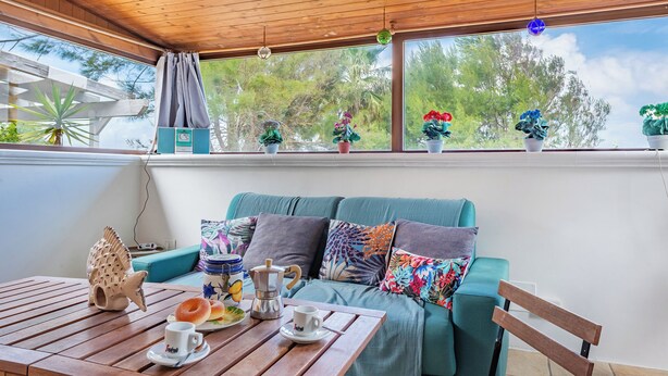 A cozy room with a wooden ceiling, a teal sofa with colorful cushions, a wooden table with a coffee pot and pastries, and a window with potted plants. - La Porta Sul Mare - Sea-View Home with Private Beach Access, Diso, Italy (Diso)