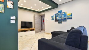A modern living room with a flat-screen TV, a dark blue sofa, and a wall with abstract art.