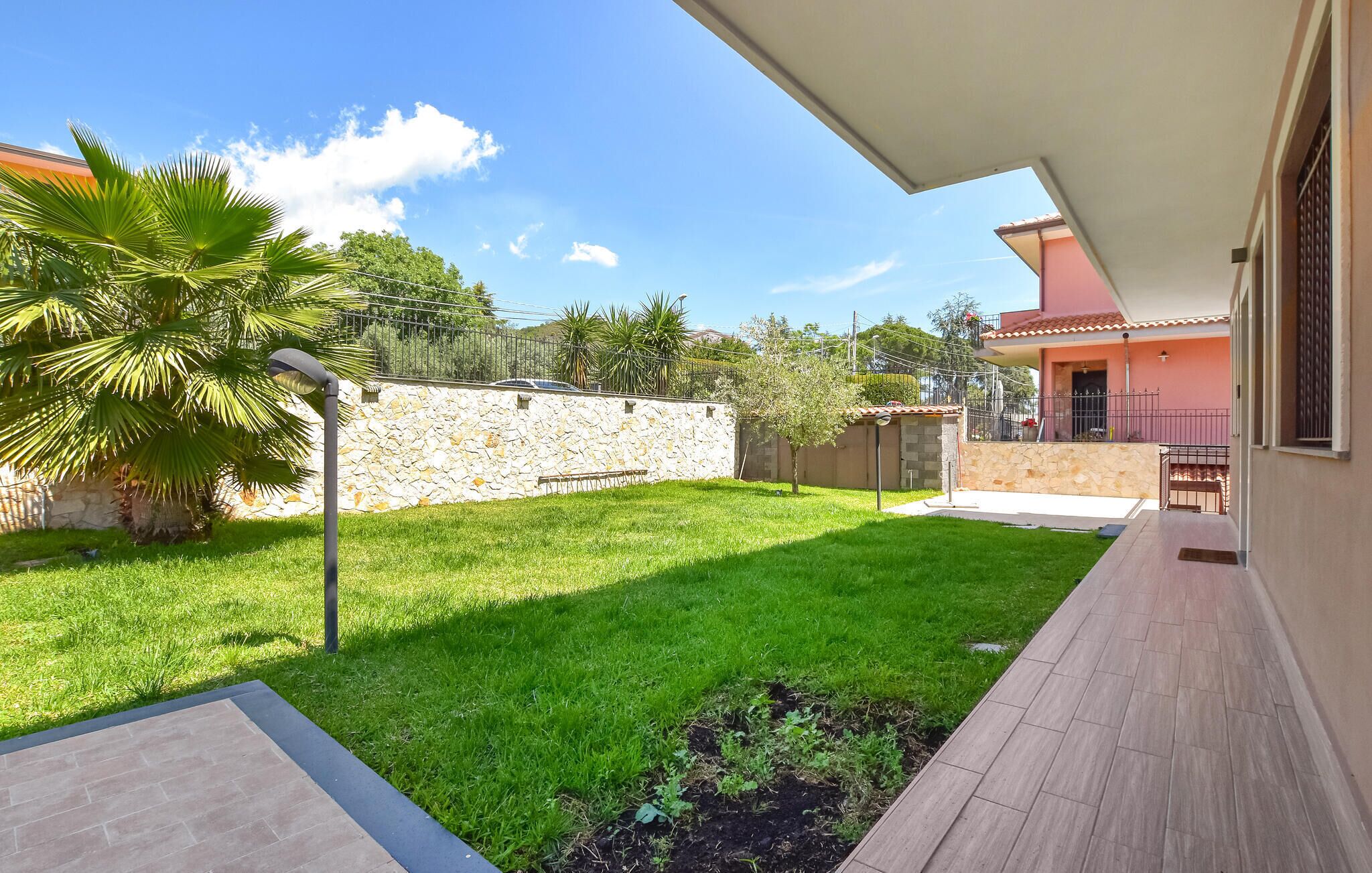 A spacious outdoor area with a well-maintained lawn, a stone wall, and a wooden deck leading to a building with a pink facade.