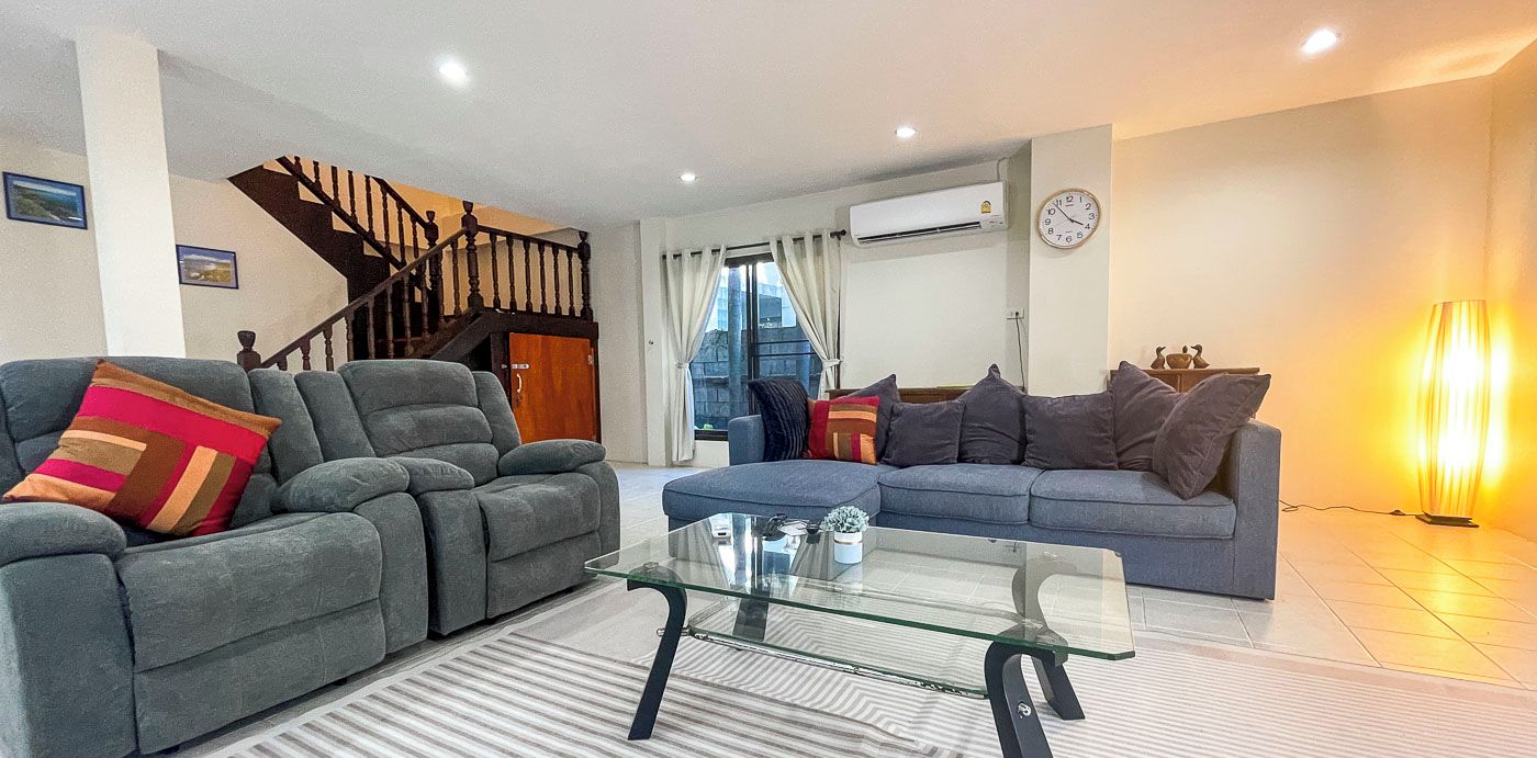 A modern living room with two sofas, a glass coffee table, and a staircase.