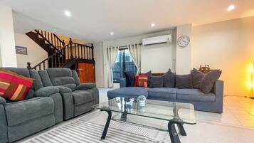 A modern living room with two sofas, a glass coffee table, and a staircase.