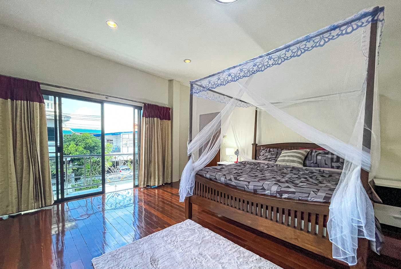 A bedroom with a four-poster bed, a large window with curtains, and a view of greenery outside.