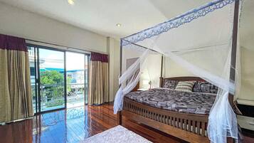 A bedroom with a four-poster bed, a large window with curtains, and a view of greenery outside.