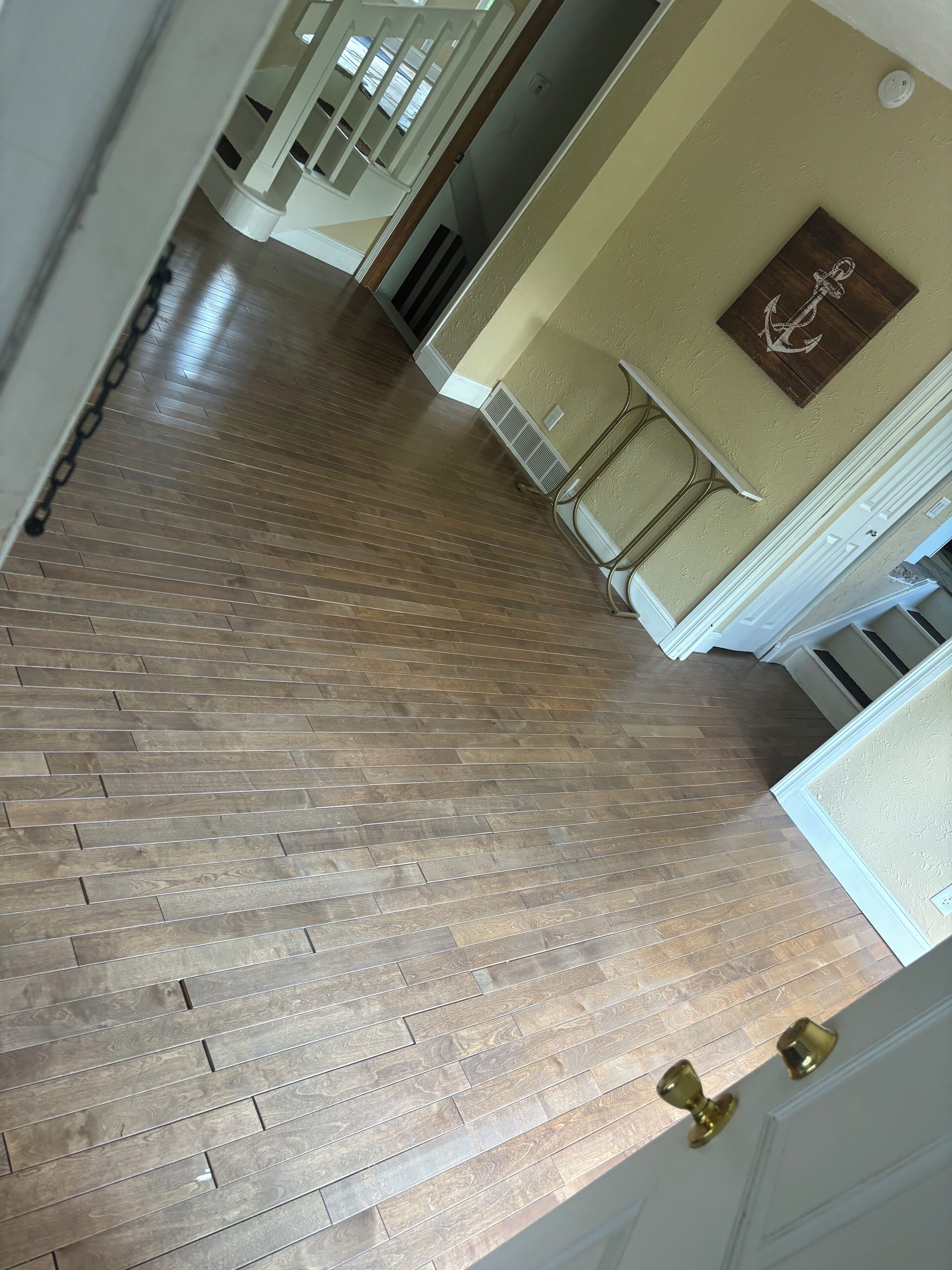 Un pasillo con suelo de madera, paredes blancas y una puerta con tiradores de latón.