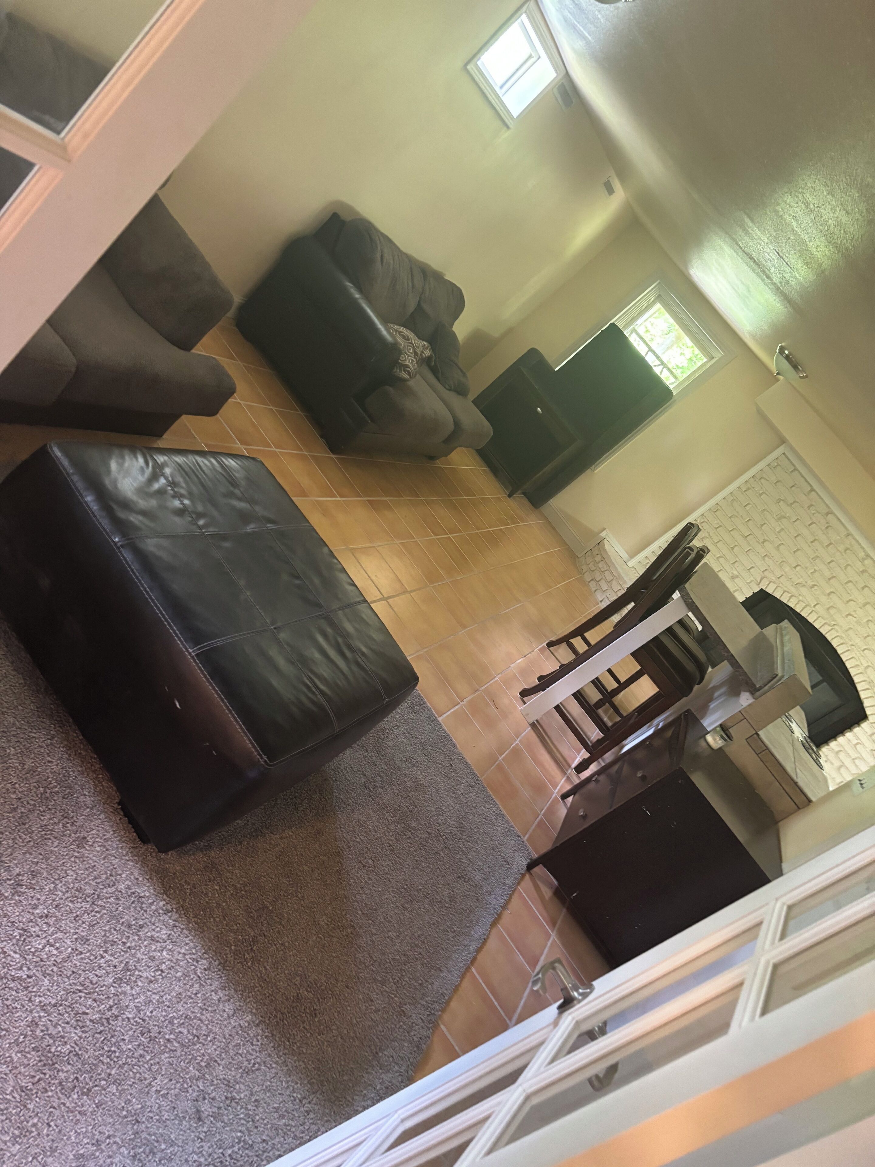 Een woonkamer met een bank, een poef en een eethoek met stoelen en een tafel.