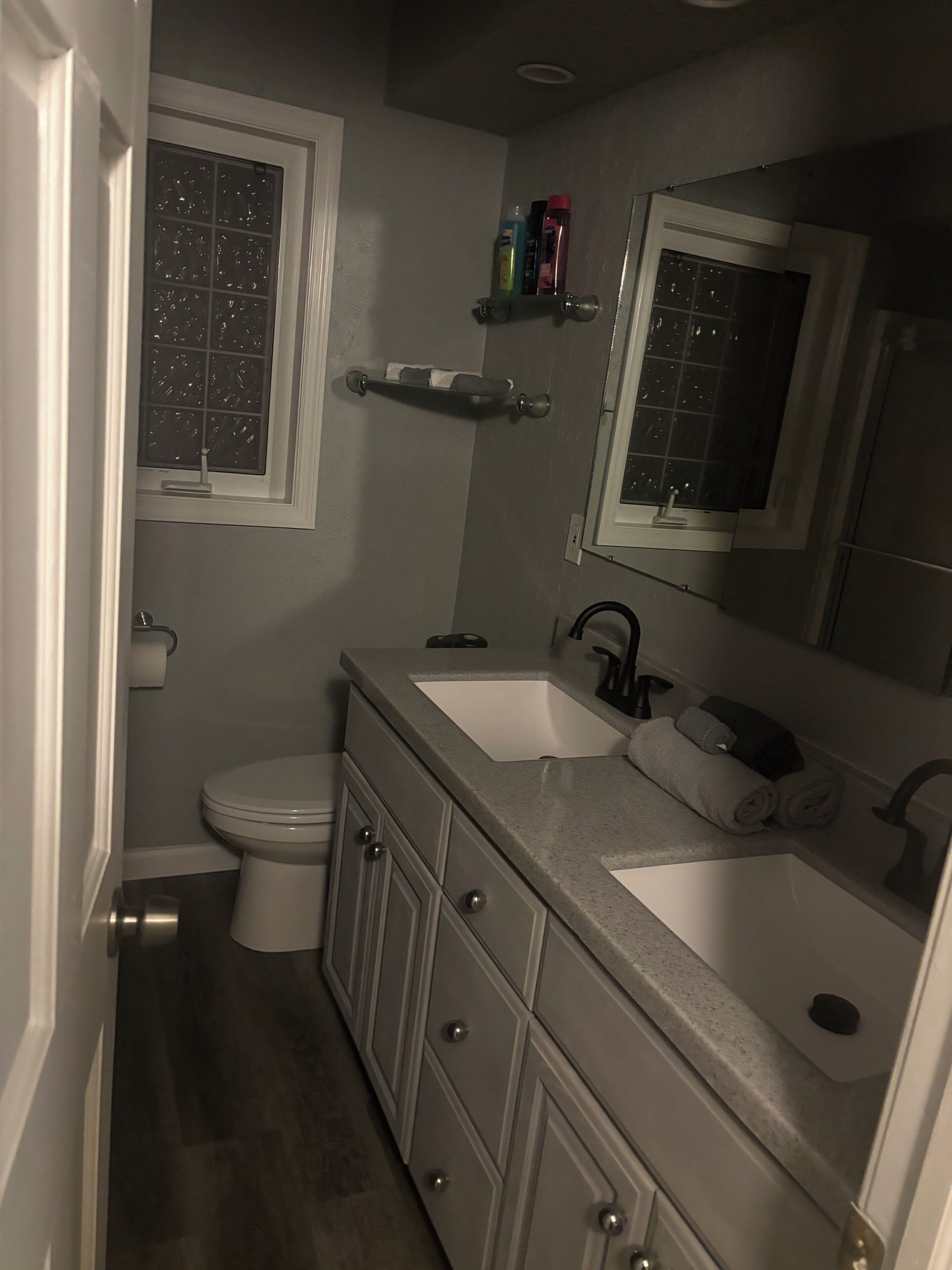 A bathroom with a toilet, two sinks, a mirror, and a window.