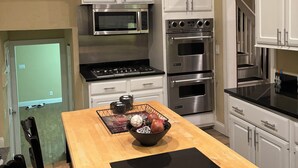 Une cuisine moderne avec des meubles blancs, des appareils en acier inoxydable, une table à manger en bois et un set de table noir.