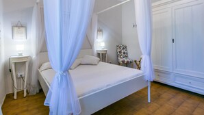 A four-poster bed with white linens, a bedside table with a lamp, a floral chair, and a wardrobe with a mirror. - Le Rocche by Interhome (Casale Marittimo)