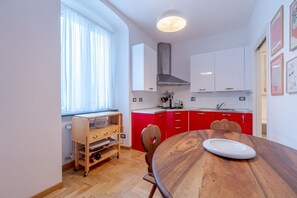 A modern kitchen with a wooden dining table, red cabinets, and a window with sheer curtains.