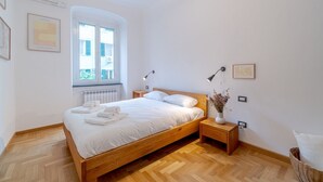 A bedroom with a wooden bed, bedside tables, a radiator, and a window with a view. - GuestHost - Genova Brignole Modern and Central Apartment (Genova)