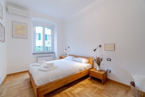 A bedroom with a wooden bed, bedside tables, a radiator, and a window with a view.
